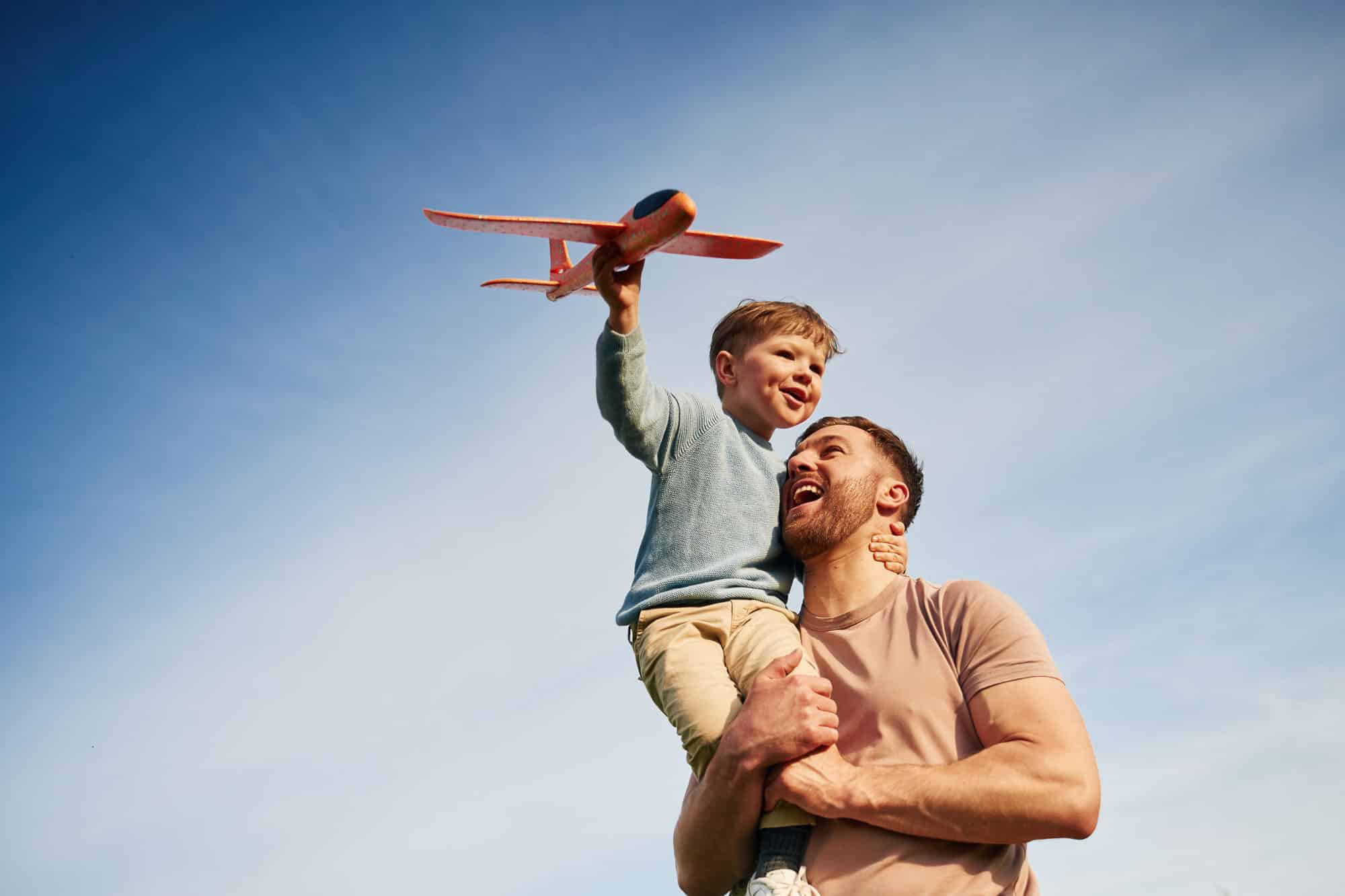 father smiling and holding his son who is playing with a toy airplane